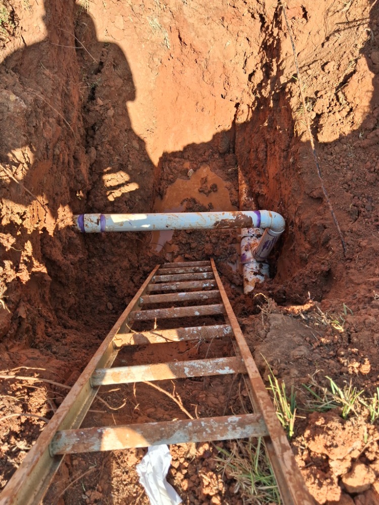 PVC sewer drain tie-in installed in an excavated trench with purple primer joints.